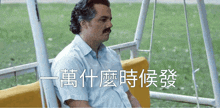 a man with a mustache is sitting on a swing with chinese writing on it