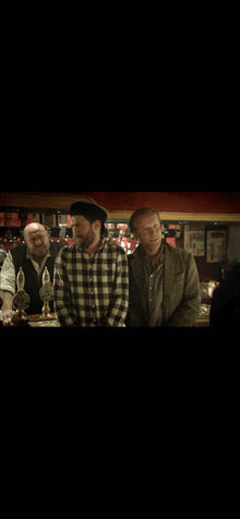 a man in a plaid shirt stands next to another man at a bar