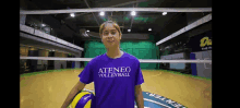 a woman wearing a purple ateneo volleyball shirt is holding a volleyball .