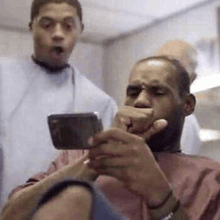 a man is taking a picture of himself with a cell phone while another man looks on .