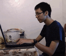 a man wearing glasses is typing on a laptop with a bag of rice in the background