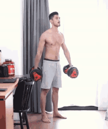 a shirtless man is lifting a pair of dumbbells in a room