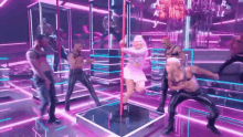 a woman in a pink dress is dancing on a pole with a group of men behind her .