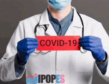 a doctor wearing a mask and gloves holds up a sign that says covid-19