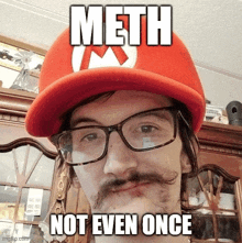 a man with glasses and a mustache is wearing a mario hat and says " meth not even once "