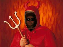 a man in a devil costume holds a trident in front of flames