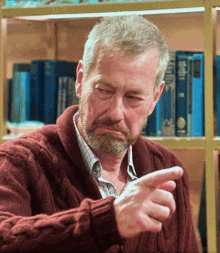 a man in a red sweater is pointing at something in front of a bookshelf