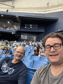 a man wearing a rays shirt sits next to a man wearing glasses