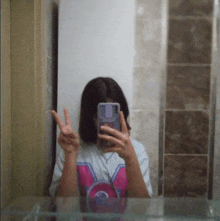 a girl is taking a picture of herself in a mirror and giving a peace sign