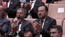 a man in a suit and tie is yawning while applauding in a crowd