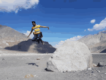 a man in a yellow and black striped shirt jumps over a large rock