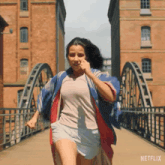 a woman is running on a bridge with a netflix logo on the bottom