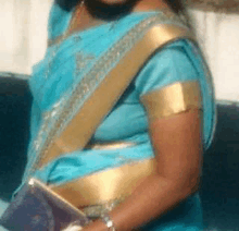 a woman in a blue and gold saree is holding a clutch bag .