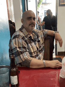 a man with a tattoo on his arm sits at a table with a bottle of beer