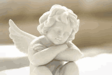 a white angel statue is sitting on a table with its head on its hands .