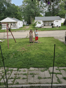 a boy and a girl are standing in a grassy yard in front of a swing set