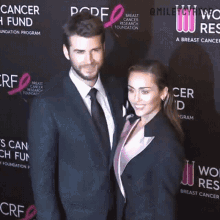 a man and a woman are posing for a picture in front of a sign that says breast cancer research foundation