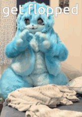 a blue stuffed animal is sitting on a bed with the words get flopped below it