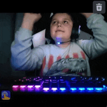 a young boy wearing headphones and a dinosaur shirt is sitting in front of a keyboard .