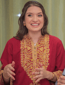 a woman wearing a red top with gold embroidery smiles with her hands outstretched