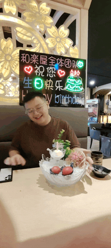 a man sits at a table with a bowl of food and a sign that says happy birthday