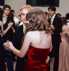 a girl in a red dress is dancing with a man in a black suit