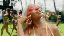 a woman in a bikini wearing sunglasses and hoop earrings is standing in front of a group of women in bikinis .