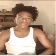 a young man wearing a white tank top is sitting in a chair .