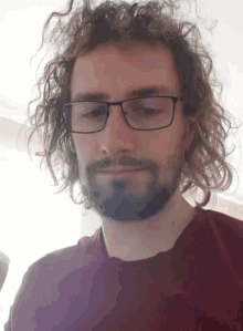 a man with curly hair and a beard is wearing glasses and a red shirt .