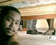 a man is standing under a bed looking at a woman 's feet in heels .