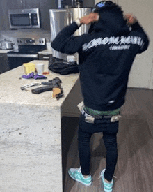 a man is standing in a kitchen wearing a black hoodie and green pants .