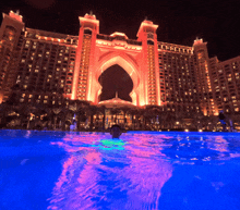 a man is swimming in a pool in front of a large building that is lit up at night