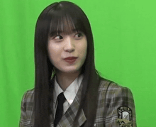 a woman in a plaid jacket and tie is standing in front of a green screen and making a funny face .