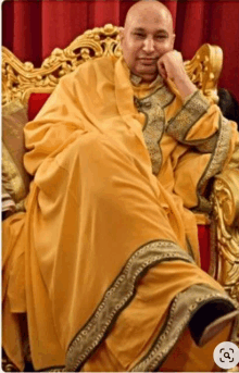 a man in a yellow robe sits in a gold chair