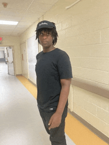 a man standing in a hallway wearing a black shirt and a hat that says ' t.m. hamilton '