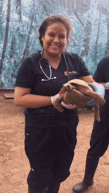 a woman in a scrub top holds a turtle and smiles