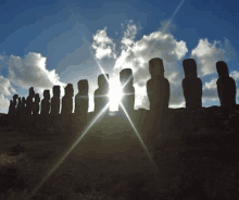 a row of statues are silhouetted against a cloudy sky with the sun shining through the clouds