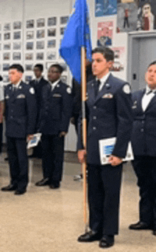 a group of men in military uniforms are standing in a line holding a blue flag .