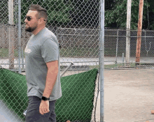 a man standing in front of a chain link fence wearing sunglasses and a shirt that says " army "