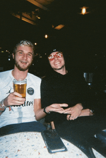 a man in an emirates shirt holds a glass of beer with another man