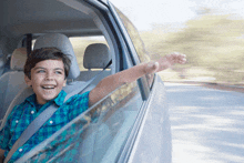 a young boy is sitting in the driver 's seat of a car with his arm out the window