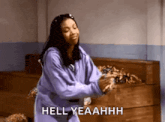 a woman in a purple sweatshirt is dancing in a room with the words hell yeahhh written below her .