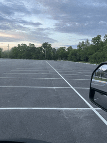 an empty parking lot with trees in the background and a rear view mirror