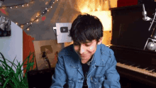 a young man in a denim jacket is sitting at a piano .