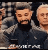 a man with a beard is sitting in a crowd looking at his cell phone and saying `` or maybe it was '' .