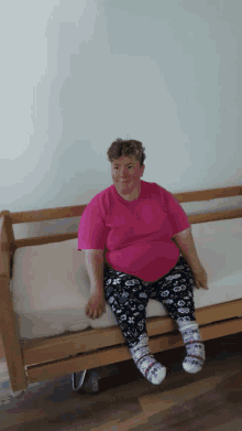 a woman in a pink shirt sits on a bed with her legs crossed