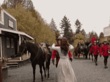 a woman in a white dress is walking down a gravel road next to a man riding a horse .