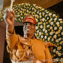 a man in a military uniform is holding a sword in front of a wreath of yellow and white flowers that says sanjo