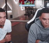 two young men are sitting in chairs in front of a tv .