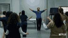 a man in a blue shirt stands in front of a group of women in orange uniforms with a netflix logo in the corner